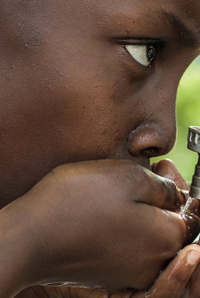 Photo of a boy drinking water from a faucet.