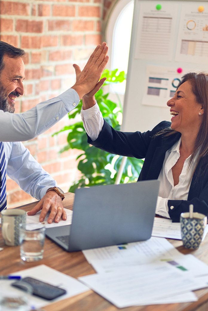 Two middle age business workers smiling and giving each other a high five at the office.