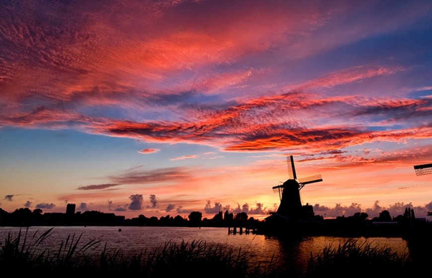 Photo of a Dutch landscape with a couple of windmills next to a canal.