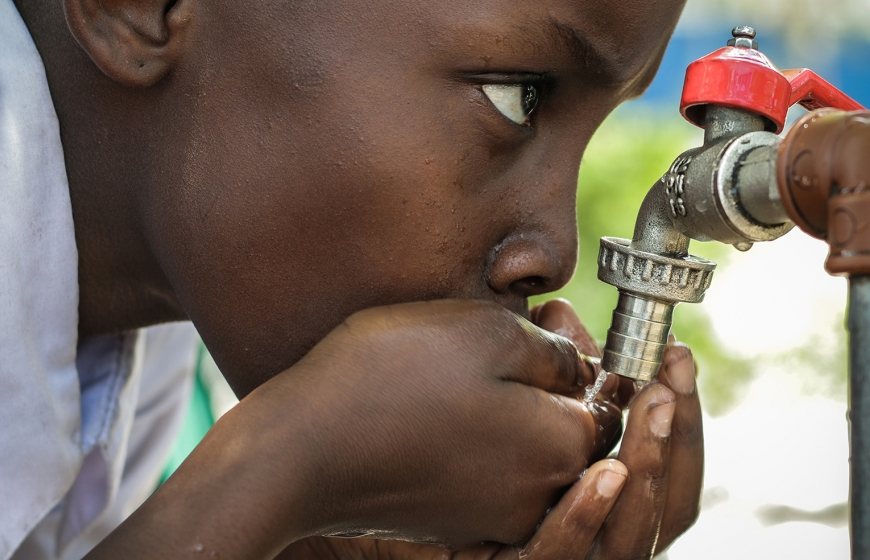 Photo of a boy drinking water from a faucet.