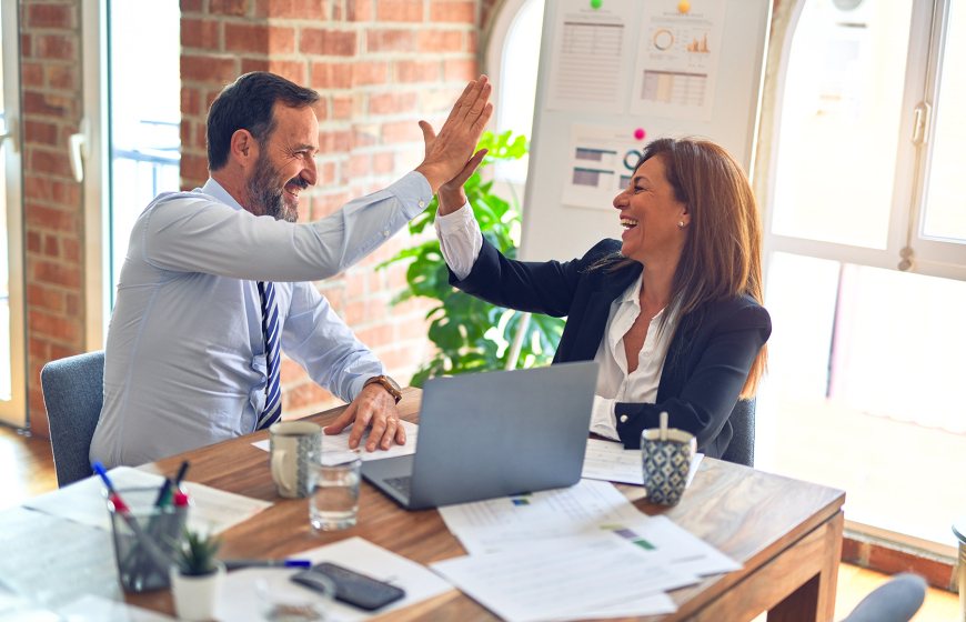 Two middle age business workers smiling and giving each other a high five at the office.