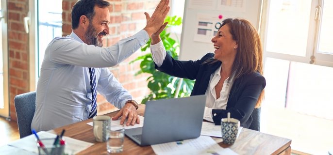 Two middle age business workers smiling and giving each other a high five at the office.