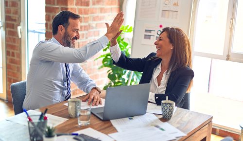 Two middle age business workers smiling and giving each other a high five at the office.